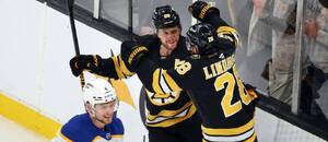 David Pastrňák a Elias Lindholm se radují po vstřelení gólu, kolem nich projíždí Bowen Byram